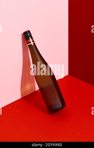 Bottle of wine leaning on the wall. Alcoholic drink on red and pink creative background with deep shadows Stock Photo