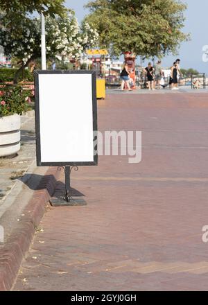 Close-up of blank white signboard on the streetside. people around. Stock Photo