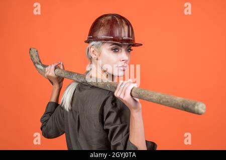 woman architect in protective helmet and boilersuit hold shovel on orange background, building Stock Photo
