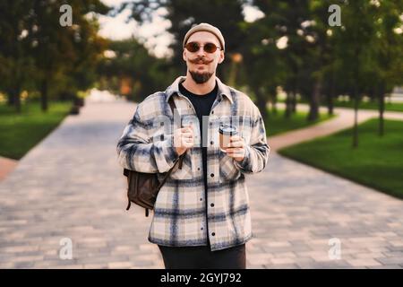 Handsome bearded stylish hipster walk around park outdoor with coffee to go while having relax time Stock Photo