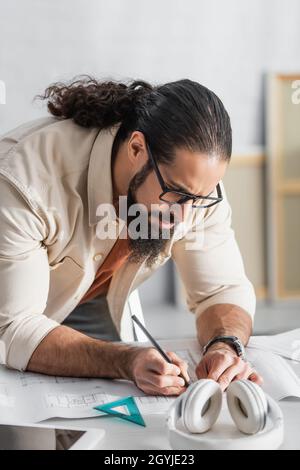 serious hispanic architect drawing on blueprint while working at home Stock Photo