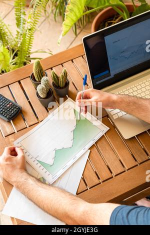 Top view of broker analyzing charts on desk with a computer while investing in stock market from outdoor home office full of plants. Stock Photo
