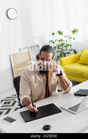 latin designer drawing on graphic tablet while working near laptop at home Stock Photo