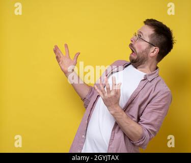 Man in shock and stupor, looks to the side with an open mouth and a strange grimace and makes an inquiring gesture with hands.  Stock Photo