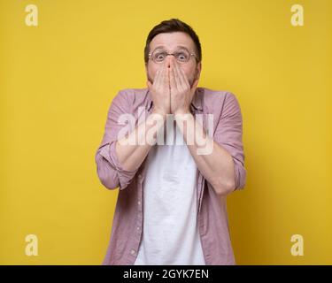 Man with glasses is shocked by a pleasant surprise, he is very surprised, covers part of face with hands and looks happily.  Stock Photo
