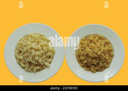 Top view cooked and uncooked macaroni on white round plate and background is bright yellow, copy space. Stock Photo