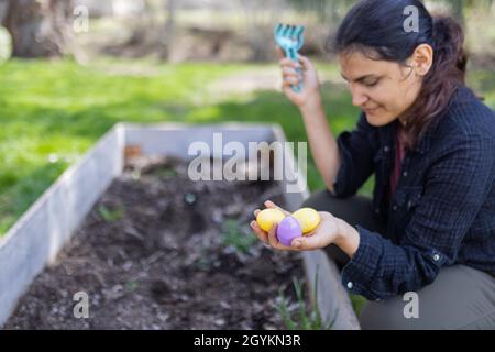 Beautiful brunette woman hiding easter eggs in an empty planter box Stock Photo