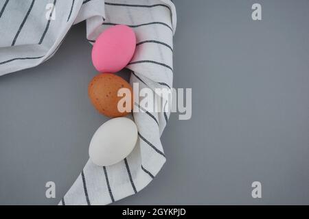 Beautiful colourful eggs, white, brown, and pink still life, food styling with pattern tea towel cloth flat lay on gray background. Stock Photo