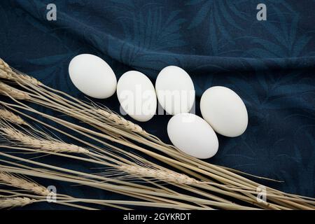 White eggs with dry wheat stems flat lay on blue charade and gray gunsmoke colored organic crumpled texture tea towel, napkin, fabric abstract. Stock Photo