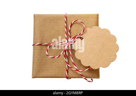 Christmas gift box with blank round note card, brown kraft paper holiday present with red white striped string tied bow isolated cutout on white backg Stock Photo