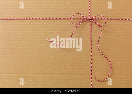 Christmas string tied in a bow on kraft paper background. Red white striped twine holiday gift decoration on brown recycled carton present wrap. Homem Stock Photo