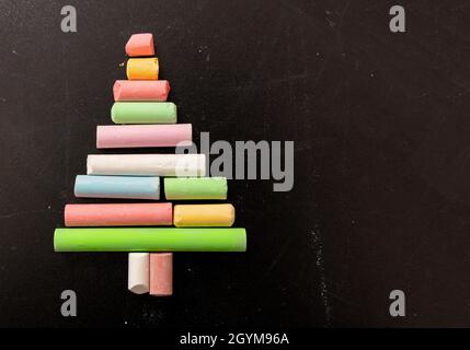 Christmas tree shape with colorful chalks on a school black board. Winter holidays for students, happy children. Empty space, xmas and New year greeti Stock Photo