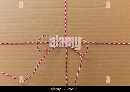 Christmas string tied in a bow on kraft paper background. Red white striped twine holiday gift decoration on brown recycled carton present wrap. Homem Stock Photo