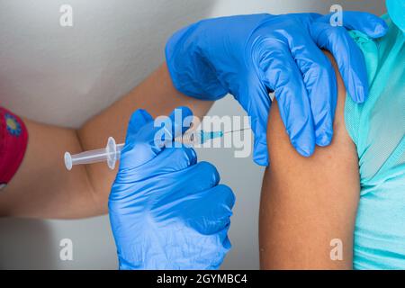children's nurse injecting arm of little brown girl. doctor's hands with rubber gloves injecting covid-19 or flu vaccine. medical concept, health and Stock Photo