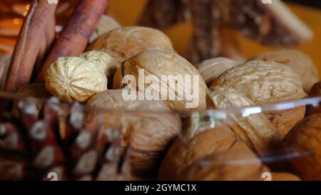 several walnuts lie with a pine cone, a peanut and cinnamon sticks in a brown glass bowl, side view, close-up Stock Photo