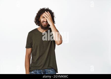 Image of frustrated young man failing, feeling upset, making facepalm from regret, standing disappointed against white background Stock Photo
