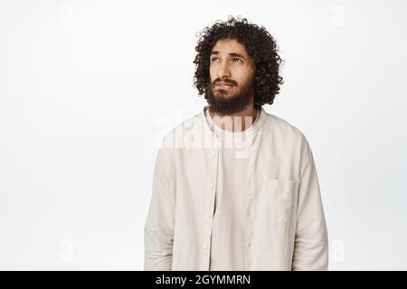 Portrait of thoughtful middle eastern man looking at upper left corner, thinking, standing over white background Stock Photo