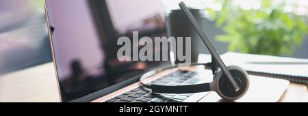 Headphones with microphone lying on laptop keyboard on desktop closeup Stock Photo