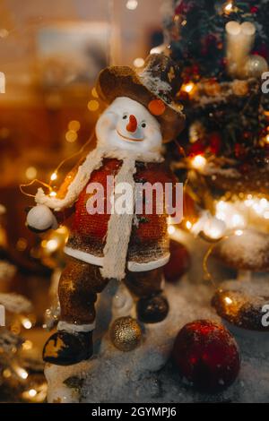 Funny winter toy snowman and Christmas tree branch with golden lights on a festive storefront. New Year and Merry Christmas decorations and a magical Stock Photo