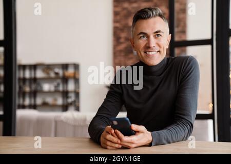 Handsome smiling man using mobile phone while sitting at home Stock Photo