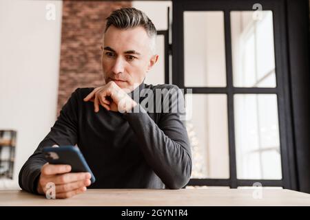 Handsome focused man using mobile phone while sitting at home Stock Photo