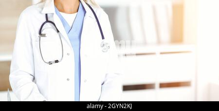 Unknown woman-doctor is typing on desktop computer at reception desk in sunny clinic. Medicine concept. Stock Photo