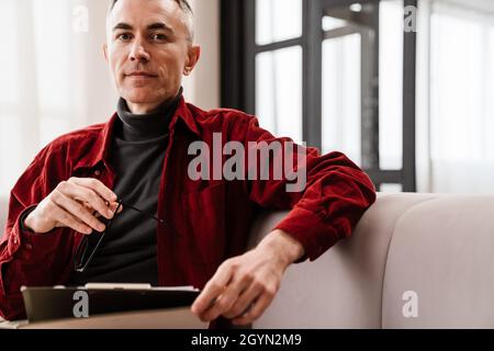 Handsome serious man working with papers while sitting on couch at home Stock Photo
