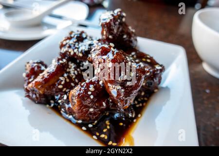 Close up of saucy baby back pork ribs on a white square plate inside an Asian restaurant Stock Photo