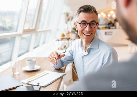 Two happy business colleagues discussing new project while sitting in cafe indoors Stock Photo