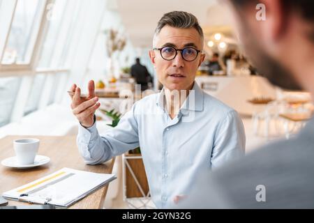 Two business colleagues discussing new project while sitting in cafe indoors Stock Photo