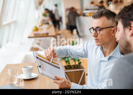 Two business colleagues discussing new project while sitting in cafe indoors Stock Photo