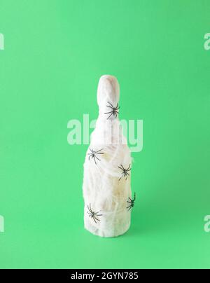 A bottle of champagne in a spider's web. Black spiders stand on the web. Green background. Halloween celebration party concept. Stock Photo
