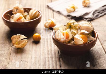 Physalis Peruvian fruits in brown bowls on a wooden background. Stock Photo