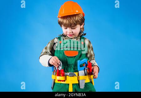 Child in helmet and in builder uniform with tool belt. Kid boy repairman with tools for building. Stock Photo
