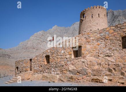 Stone walls of small medieval Arabian fort under tall mountain cliffs. Fortress in Bukha, Musandam peninsula, Oman. Hot, hazy day in Arabian desert. Stock Photo