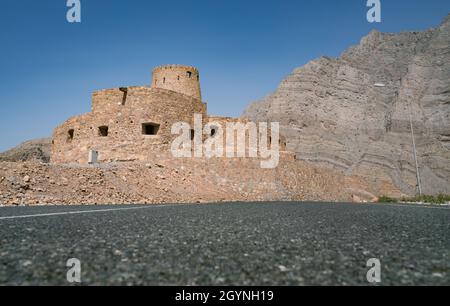 Stone walls of small medieval Arabian fort under tall mountain cliffs. Fortress in Bukha, Musandam peninsula, Oman. Hot, hazy day in Arabian desert. Stock Photo