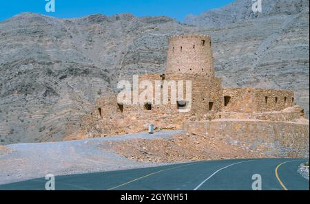 Stone walls of small medieval Arabian fort under tall mountain cliffs. Fortress in Bukha, Musandam peninsula, Oman. Hot, hazy day in Arabian desert. Stock Photo