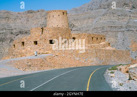 Stone walls of small medieval Arabian fort under tall mountain cliffs. Fortress in Bukha, Musandam peninsula, Oman. Hot, hazy day in Arabian desert. Stock Photo