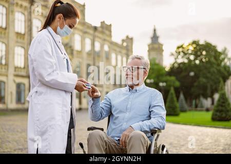 Female doctor wearing protective face mask measuring pulse rate and oxygen levels using fingertip pulse oximeter Stock Photo