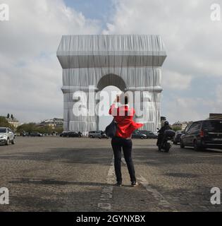 Woman uses a smartphone to photograph the Arc de Triomphe wrapped in silver-blue fabric fastened with red ropes in the Place Charles de Gaulle in Paris, France. The Arc de Triomphe was wrapped for two weeks being converted an the artwork as it was designed by Christo and Jeanne-Claude in September 2021. Stock Photo