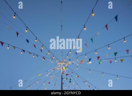 Garland with colorful pennants and light bulbs on pole over blue sky. Outdoors party background Stock Photo