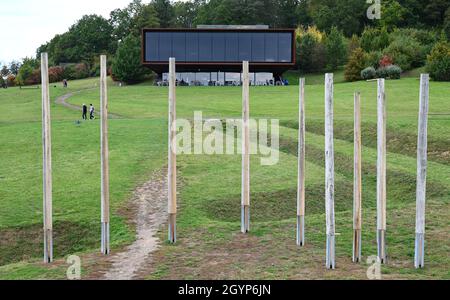 Hessen, Germany. 08th Oct, 2021. 08 October 2021, Hessen, Glauburg: Behind a group of enigmatic wooden posts standing on the edge of the reconstructed burial mound from the time of the Celts on the Glauberg, the museum building can be seen. In 1994, a research team had begun excavations and discovered, among other things, the now world-famous statue of the 'Celtic Prince of the Glauberg'. The Celtic settlement in the Wetterau region is to become a Unesco World Heritage Site. The federal states have to submit their proposals for the national preselection procedure to the Conference of Ministers Stock Photo