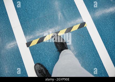 Man feet walking on blue floor in mall. Bounding lines to keep distance. Closeup Stock Photo