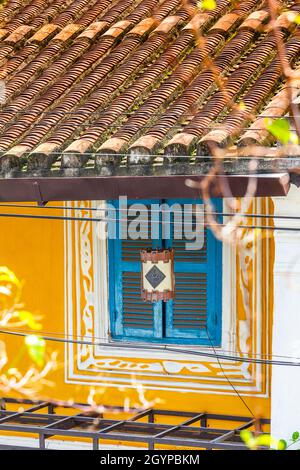 Hoi An architecture with yellow building, turquoise window shutters, white paint design and distinctive tile roof. Stock Photo