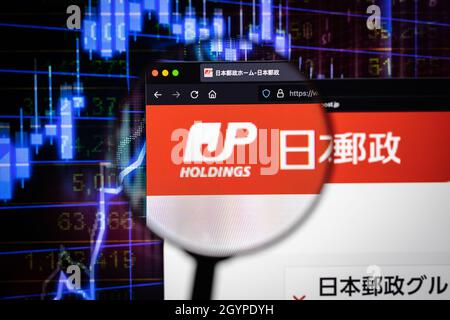 Japan Post Holdings company logo on a website with blurry stock market graphs in the background, seen on a computer screen through a magnifying glass. Stock Photo