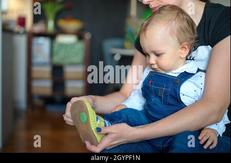 Mother sitting on a sofa and putting on the child's shoes Stock Photo