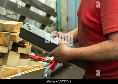 Worker with metal. The guy holds a steel part. Hard work in a metalworking workshop. Creation of steel construction. Stock Photo