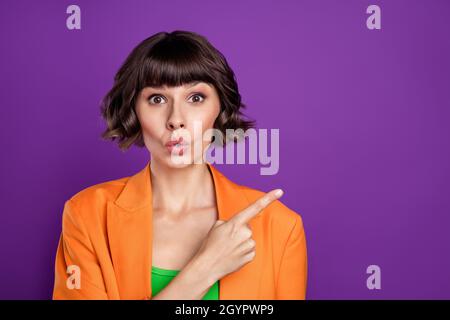 Photo of sweet impressed young woman dressed orange blazer pointing finger empty space isolated purple color background Stock Photo