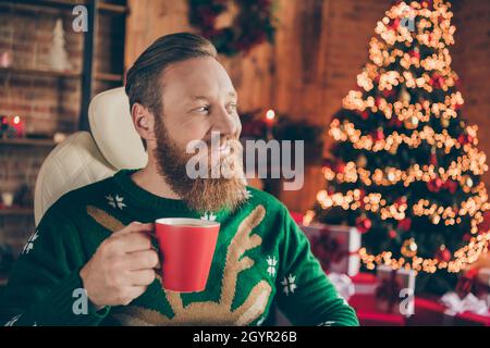 Photo of nice curious bearded ginger man sit desk hold coffee cup rest wear pullover decorated office indoors Stock Photo