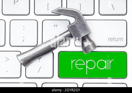 Small steel hammer lies on the keyboard, which has a green key labeled REPAIR. Hardware service concept. Stock Photo